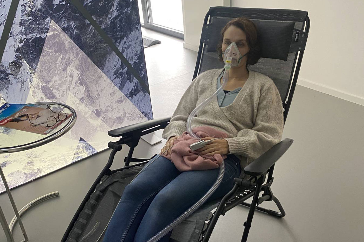 Eine Anwenderin bei SanitasVital die im Liegestuhl liegt und ein Höhentraining macht. Sie hat eine Maske vor dem Mund und der Nase, durch die Sie die Höhenluft atmet.